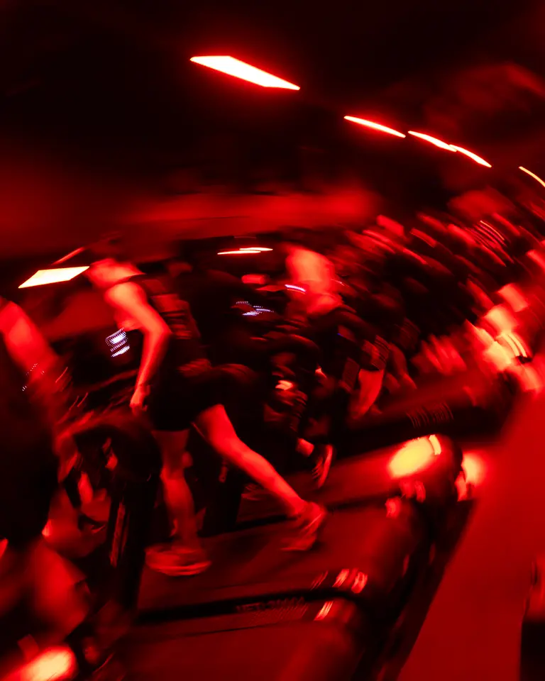 Personas corriendo en caminadoras en movimiento bajo luz roja