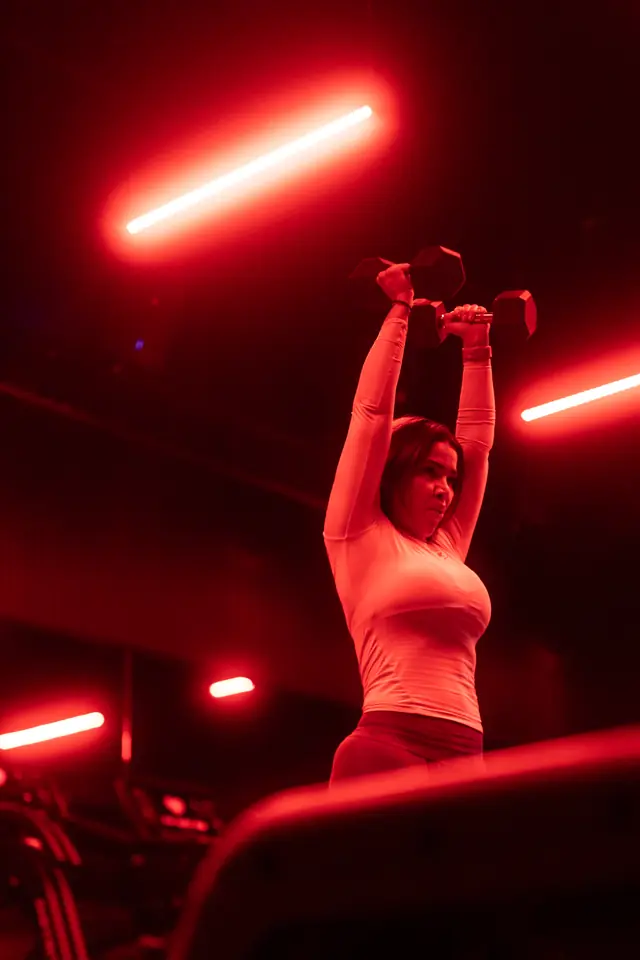 Mujer haciendo press sobre la cabeza bajo luz roja